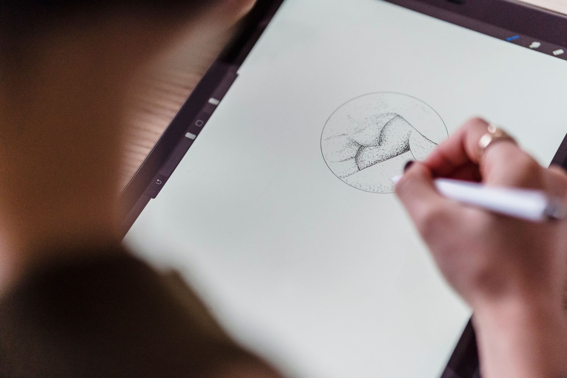 main tenant un stylet qui dessine au pointillé une forme dans un cercle sur l'écran d'une tablette