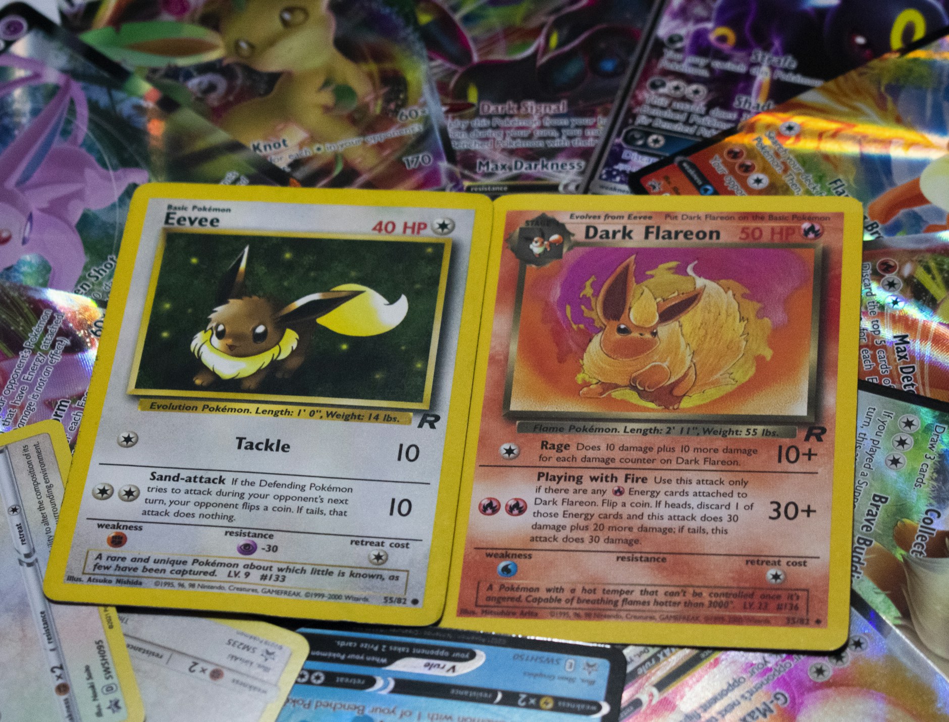 deux cartes Pokémon anciennes de l'extension Team Rocket, Évoli et Pyroli obscur, posées côte à côte sur un tas de cartes holographiques