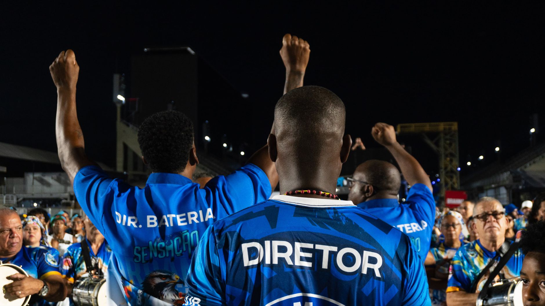directeurs de bateria en maillots bleus, poings levés, dos au photographe, au milieu des percussionnistes sur l'avenue du Sambódromo de Rio la nuit