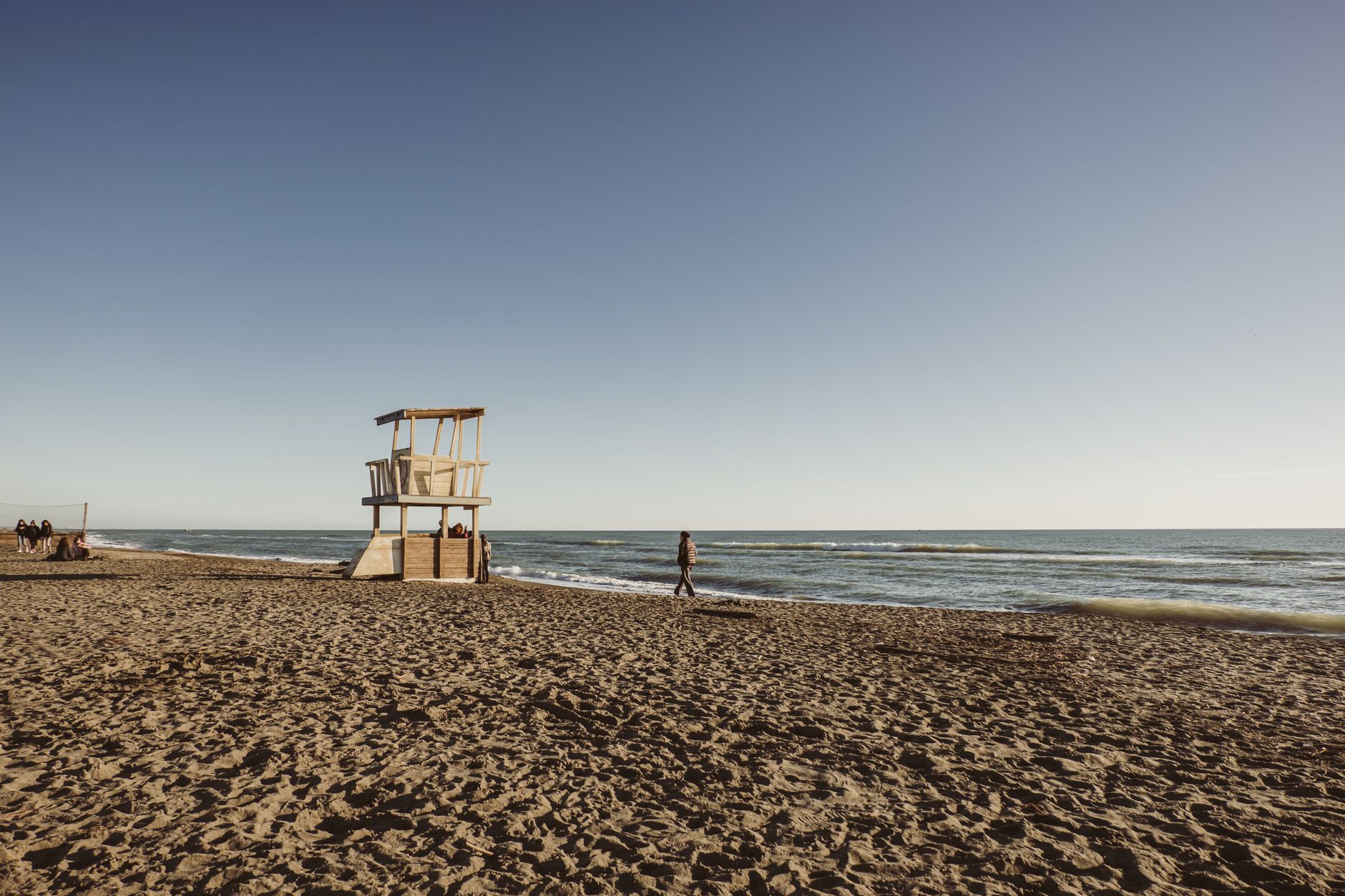 plage déserte sous un ciel dégagé en fin de saison, une personne marchant seule au bord de l'eau